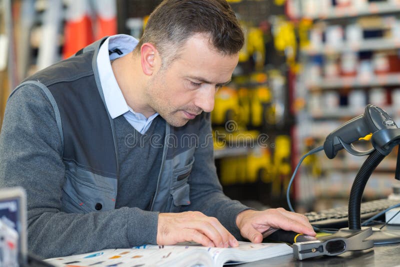 Worker in Hardware Store Looking Up Reference in Catalogue Stock Photo
