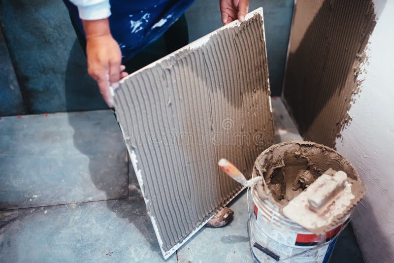 Worker Installing Bathroom Ceramic Floor Tiles, Adding Flexible Cement Adhesive with Comb Trowel