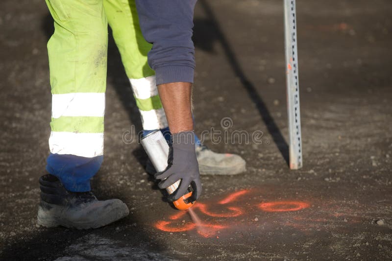 Worker Marks a Spot on Asphalt with Florescent Spray Paint Stock Photo
