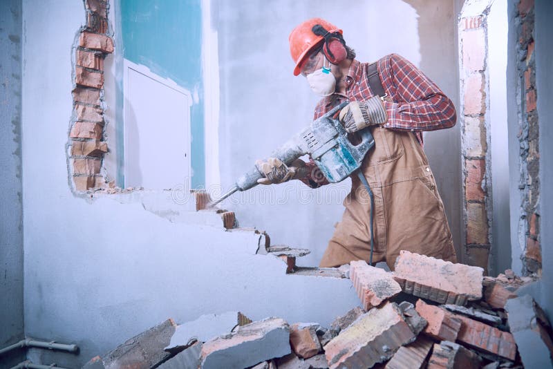 Worker with demolition hammer breaking interior wall