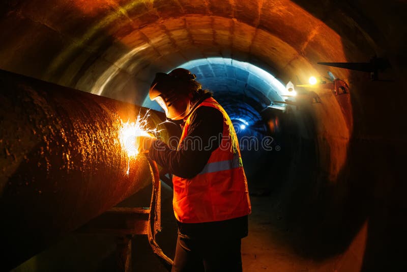Worker in protective mask welding pipe in tunnel stock image