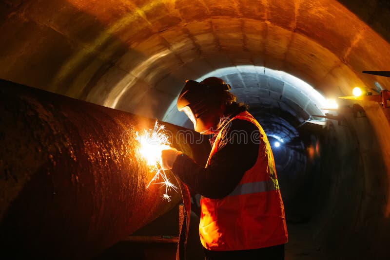 Worker in protective mask welding pipe in tunnel stock photography