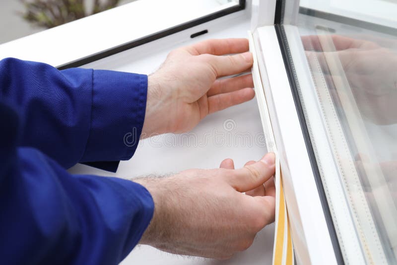 Worker putting rubber draught strip onto window indoors, closeup