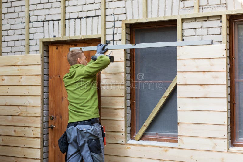 Worker restoring old brick house facade with new wooden planks