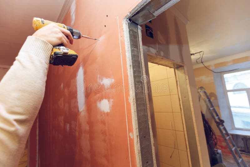 Worker is screwing the drywall by gun to the plasteboard wall in apartment is inder construction, remodeling royalty free stock images Worker is screwing the drywall by gun to the plasteboard wall in apartment is inder construction, remodeling royalty free stock images