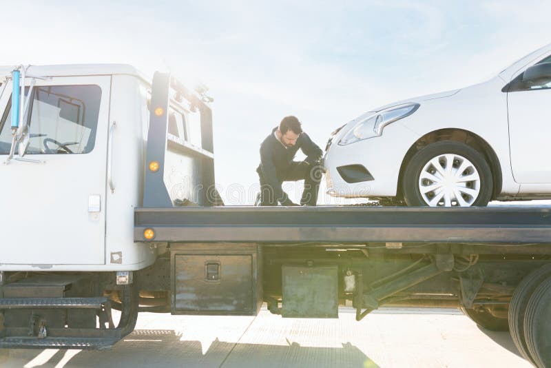 Worker securing that the car is safe on the tow truck platform stock photo
