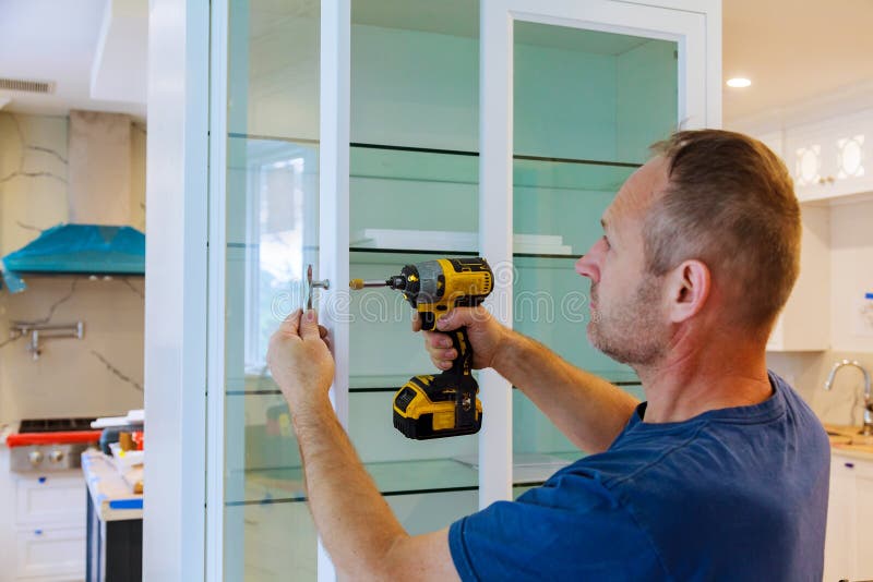 Worker Sets a New Handle on the White with a Screwdriver Installing Kitchen