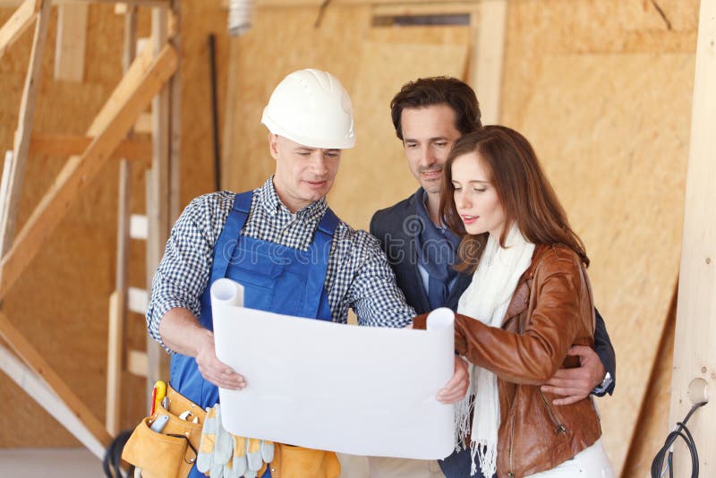 Worker shows house design plans to a young couple at construction site