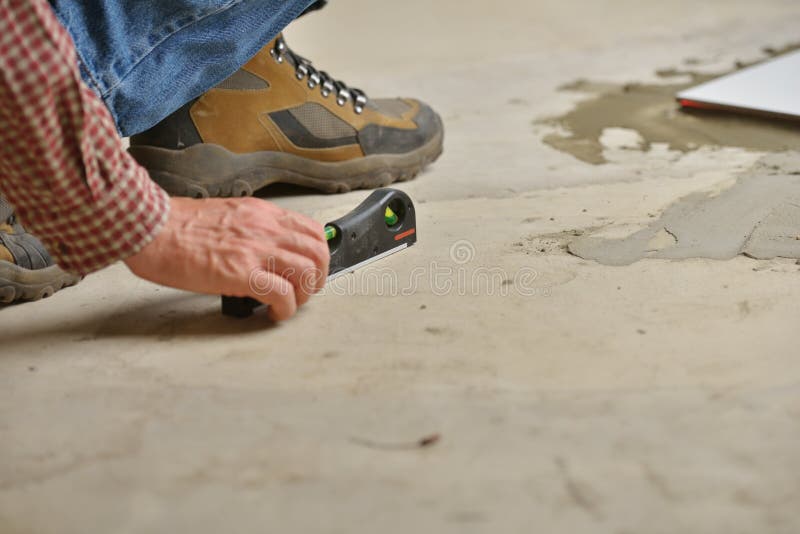 Worker checking the surface using spirit level during the tiled floor installation. Worker checking the surface using spirit level during the tiled floor installation