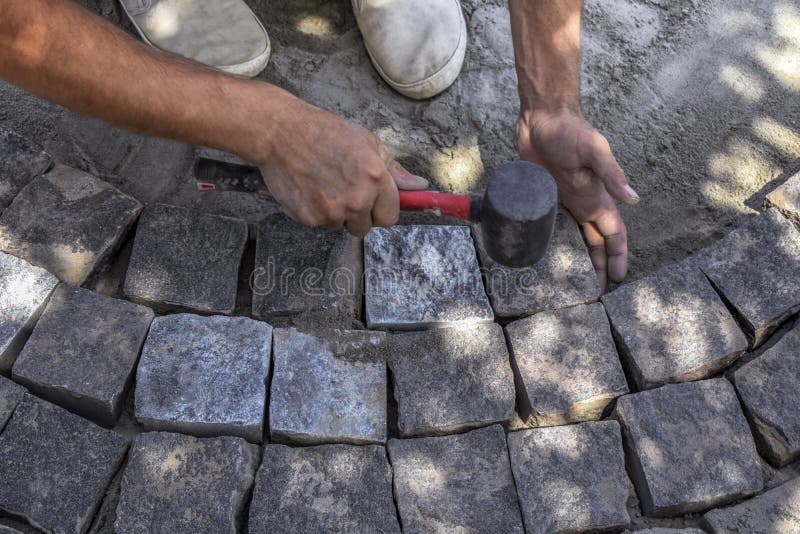 The worker stacks granite natural stones in a circle, repairing the paving surface. The process of laying paving slabs with a stock photography