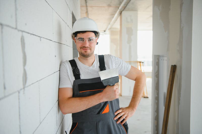 Worker in uniform plastering wall with putty knife indoors stock photos