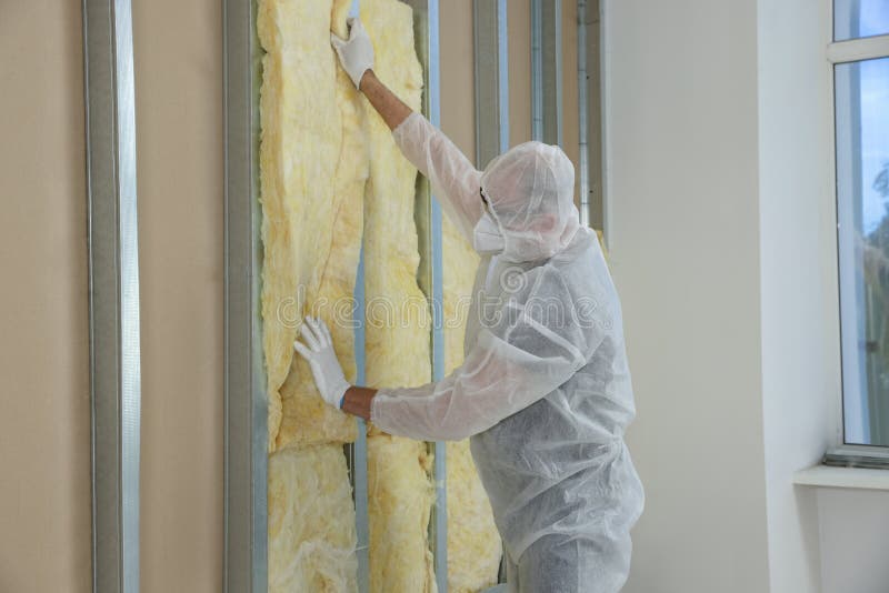 Worker in uniform and respiratory mask insulating wall indoors royalty free stock photography