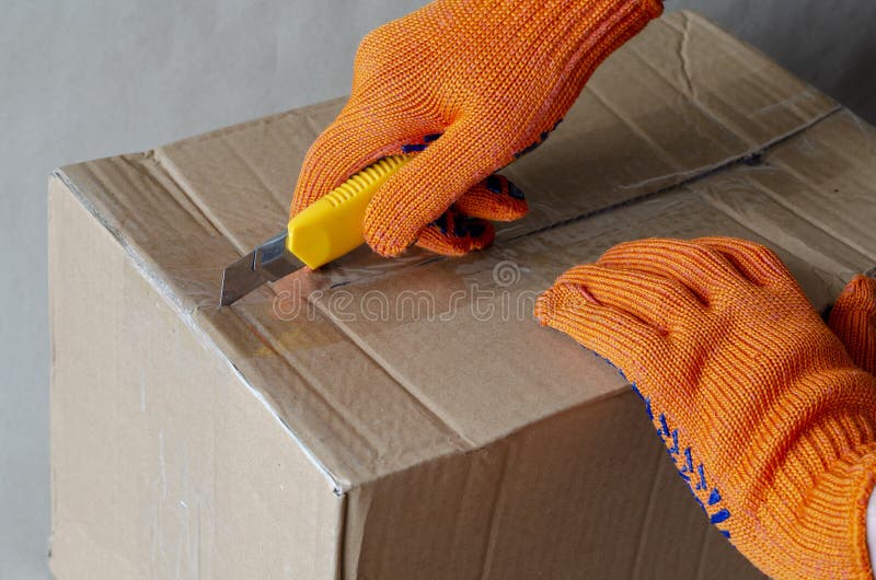 A Worker Wearing Protective Gloves Opens a Cardboard Box Stock Photo
