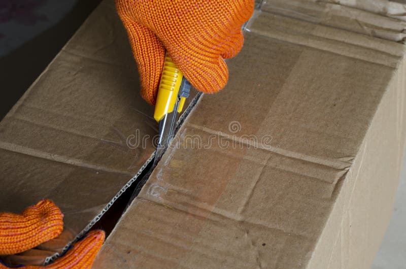 A Worker Wearing Protective Gloves Opens a Cardboard Box Stock Photo