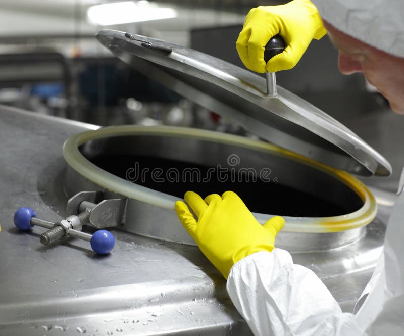 Worker in yellow gloves opening industrial process tank