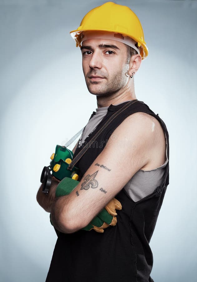 Worker. Young woker with yellow helmet,gloves and goggles posing for camera in on blue background Worker. Young woker with yellow helmet,gloves and goggles posing for camera in on blue background