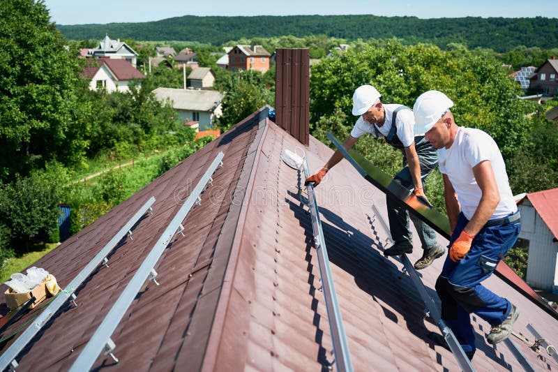 Workers building solar panel system on roof of house. Installers carrying photovoltaic solar module royalty free stock photography