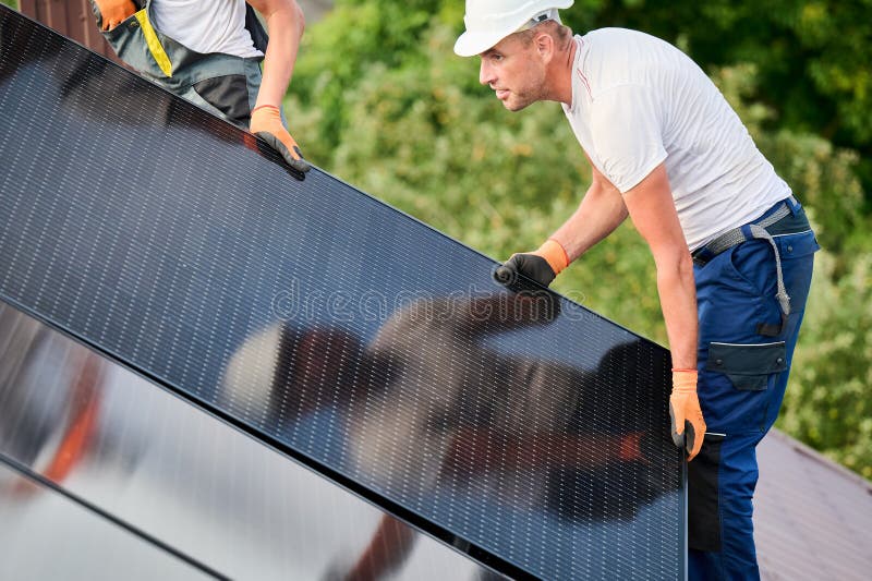 Workers building solar panel system on roof of house. Installers carrying photovoltaic solar module stock images
