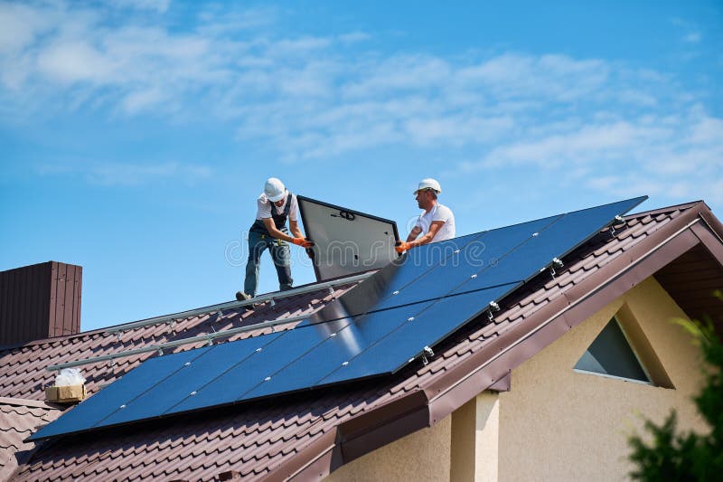 Workers building solar panel system on roof of house. Installers carrying photovoltaic solar module stock photography