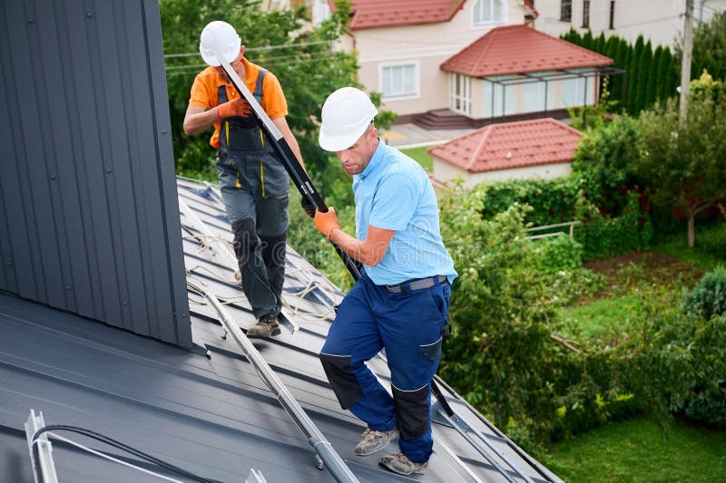 Workers building solar panel system on roof of house. Installers carrying photovoltaic solar module stock photos