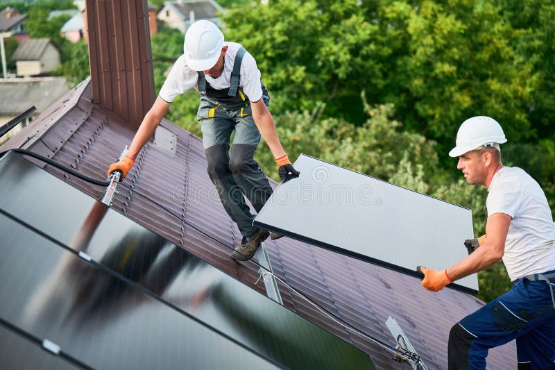 Workers building solar panel system on roof of house. Installers carrying photovoltaic solar module stock photography
