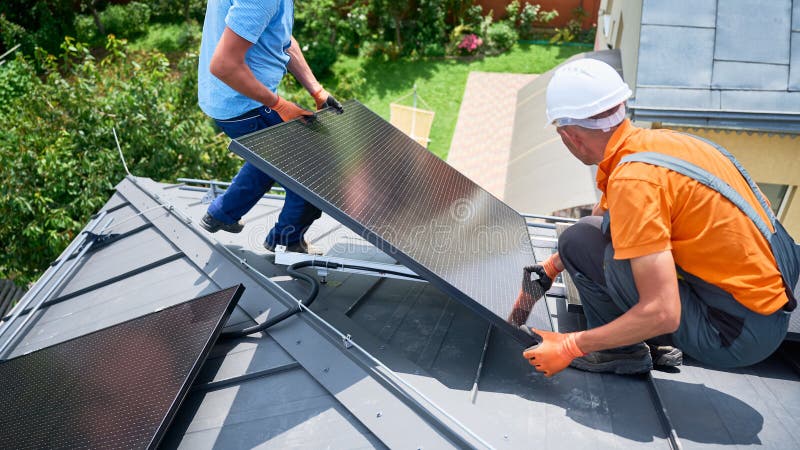 Workers building solar panel system on roof of house. Men installing photovoltaic solar module royalty free stock image