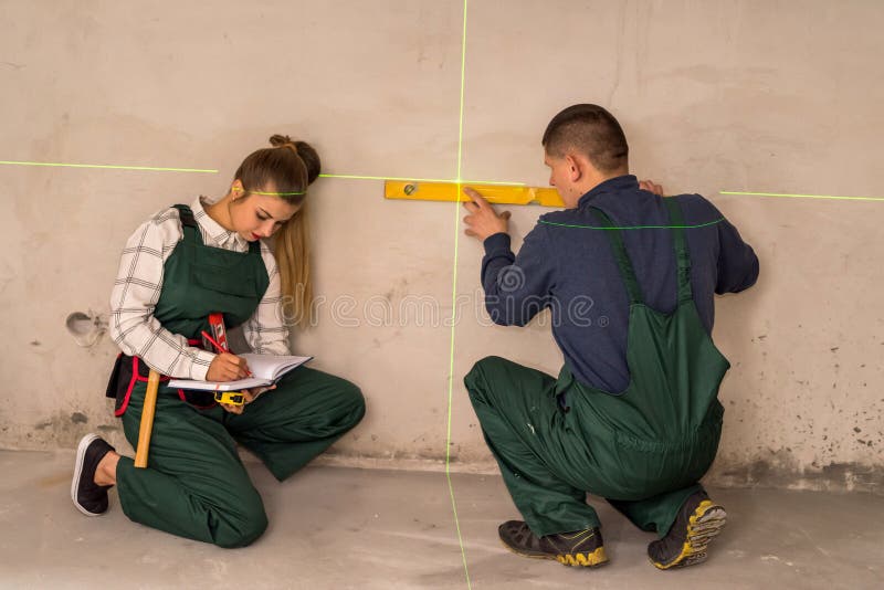 Workers checking walls with laser level tool.