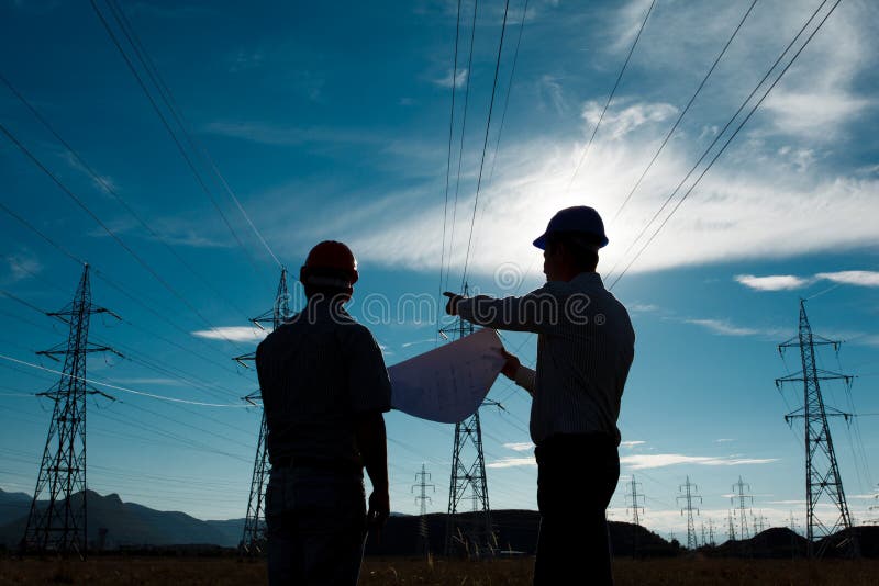 Silhouette of two engineers standing at electricity station, discussing plan. Silhouette of two engineers standing at electricity station, discussing plan