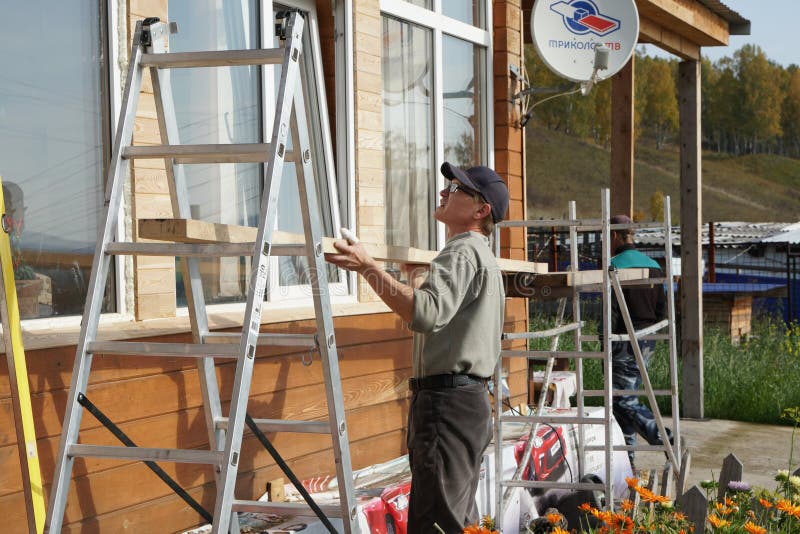 Workers install scaffolding against the wall of a wooden house on a sunny autumn day stock photography