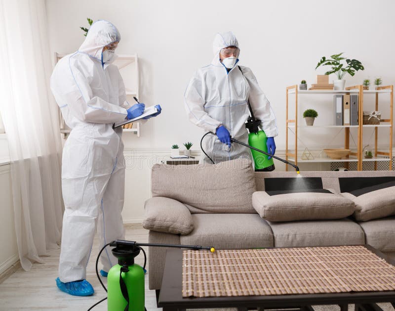 Workers wearing virus protective suits disinfecting home surfaces with spray chemicals to prevent the spreading of the coronavirus