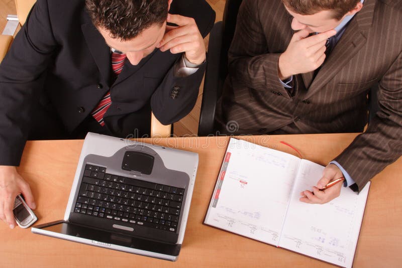 2 obchodného muži pracujú na notebook, ktorá sedí pri pulte s kalendár a mobilný telefón.