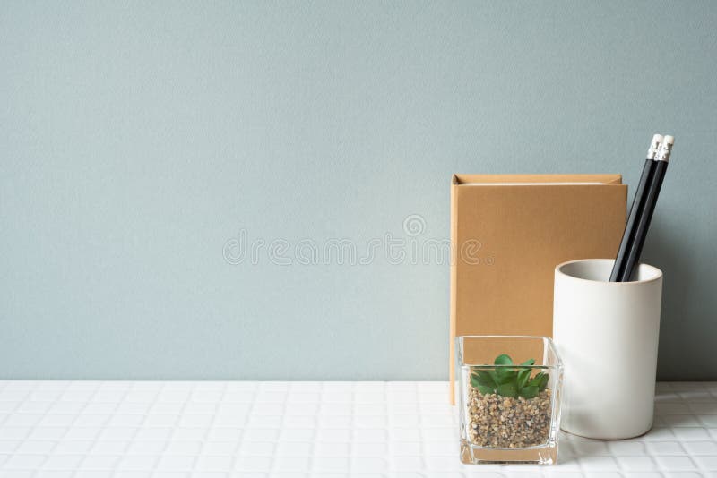 Working desk with notebook, pencil holder, potted plant on white tile desk. gray wall background. studio shot