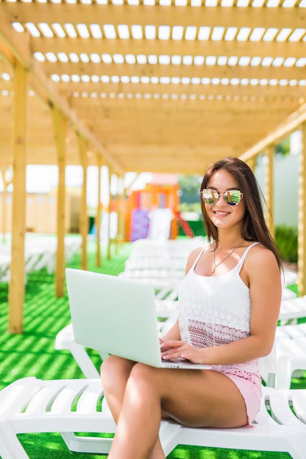 Working even on vacation. Attractive young woman in sunglasses and hat is lying on a chaise-longue near swimming pool with laptop. stock photos Working even on vacation. Attractive young woman in sunglasses and hat is lying on a chaise-longue near swimming pool with laptop. stock photos