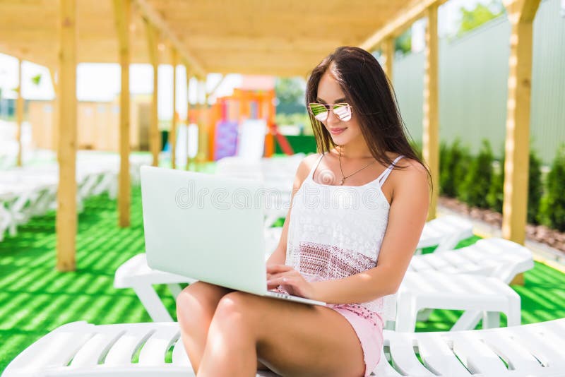 Working even on vacation. Attractive young woman in sunglasses and hat is lying on a chaise-longue near swimming pool with laptop. royalty free stock photos Working even on vacation. Attractive young woman in sunglasses and hat is lying on a chaise-longue near swimming pool with laptop. royalty free stock photos