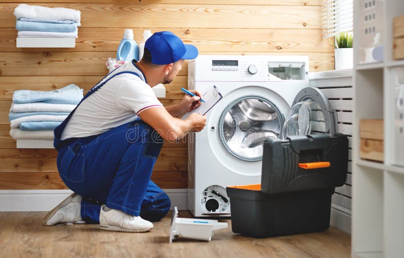 Working man plumber repairs washing machine in laundry