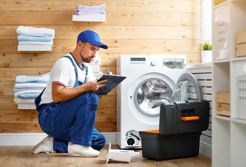 Working man plumber repairs washing machine in laundry