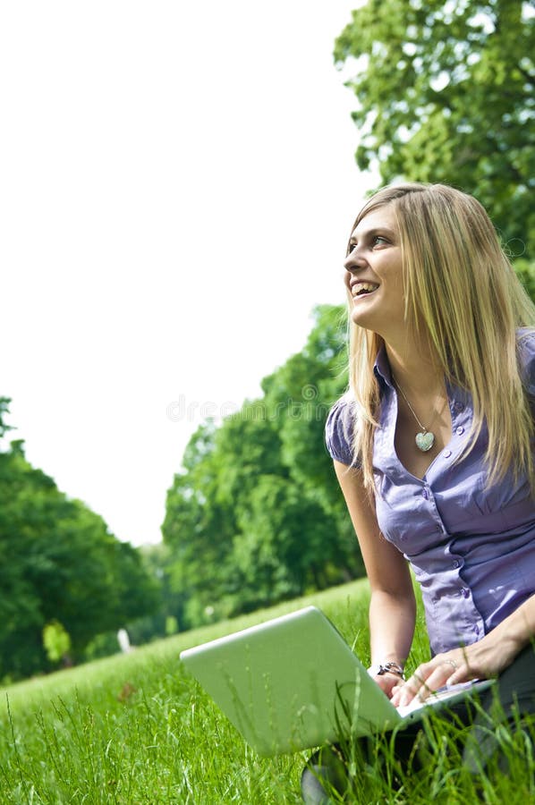 Young blond woman working with netbook outdoors in park on grass. Young blond woman working with netbook outdoors in park on grass