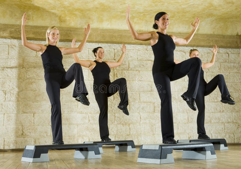 A group of women exercising in the fitness club. They're smiling and have upraised hands and one leg. Low angle view. A group of women exercising in the fitness club. They're smiling and have upraised hands and one leg. Low angle view.