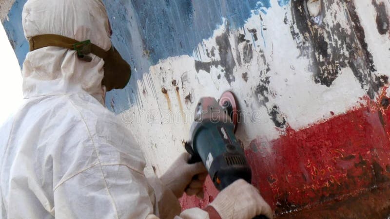 Working people tear off paint on metal in repairs process at shipyard.