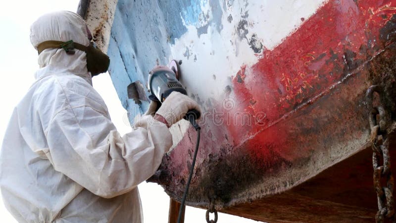 Working people tear off paint on metal in repairs process at shipyard.