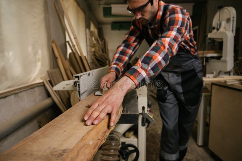 Working process in the carpentry workshop. A man in overalls uses sthicknessing planer machine in a carpentry workshop. Profession, carpentry, woodwork and people concept