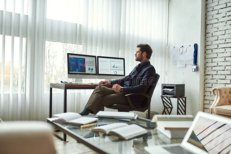 Working with statistical data. Young businessman, financial analyst sitting in the modern office, looking at graphs and stock photo