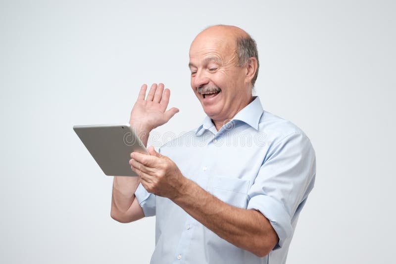 Cheerful mature european man chatting with his friends online using tablet computer royalty free stock images Cheerful mature european man chatting with his friends online using tablet computer royalty free stock images