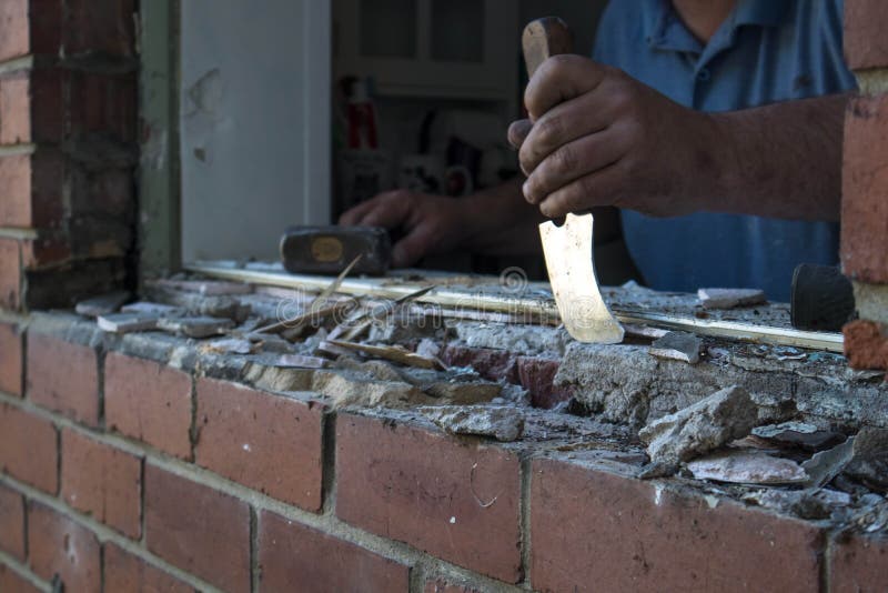 Workman removing excess mortar from a window opening in a brick wall during renovations