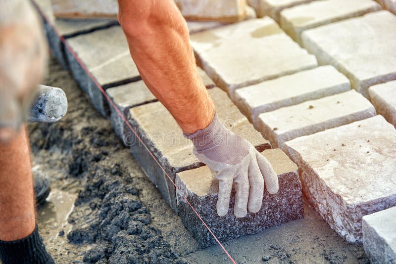 A Workman`s Gloved Hands Use a Hammer To Place Stone Pavers. Worker