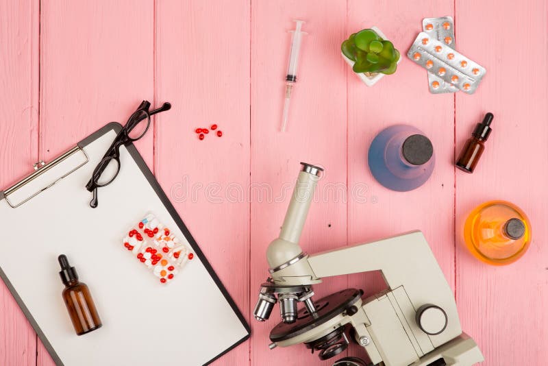 Workplace scientist doctor - microscope, pills, syringe, eyeglasses, chemical flasks with liquid, clipboard on pink wooden table royalty free stock image Workplace scientist doctor - microscope, pills, syringe, eyeglasses, chemical flasks with liquid, clipboard on pink wooden table royalty free stock image