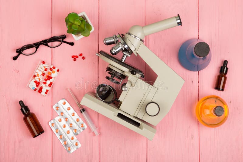 Workplace scientist doctor - microscope, pills, syringe, eyeglasses, chemical flasks with liquid on pink wooden table royalty free stock photography Workplace scientist doctor - microscope, pills, syringe, eyeglasses, chemical flasks with liquid on pink wooden table royalty free stock photography