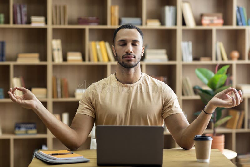 Workplace stress management. Calm arab man meditating with closed eyes in front of laptop, sitting at desk at home stock photo
