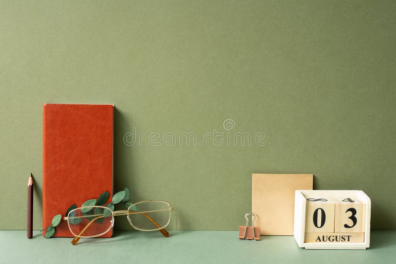 Workspace diary note, calendar, notepad, clip, pencil, eyeglasses, eucalyptus leaf on green desk. khaki wall background. studio shot