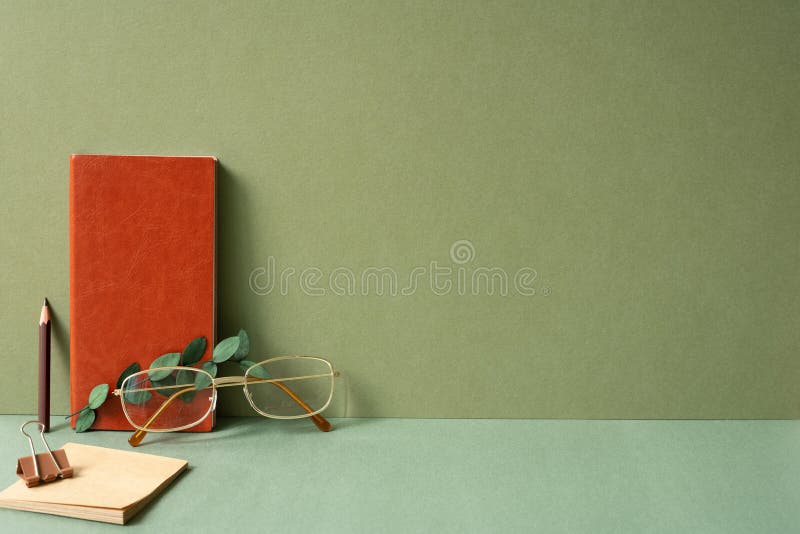 Workspace diary note, notepad, clip, pencil, eyeglasses, eucalyptus leaf on green desk. khaki wall background. studio shot